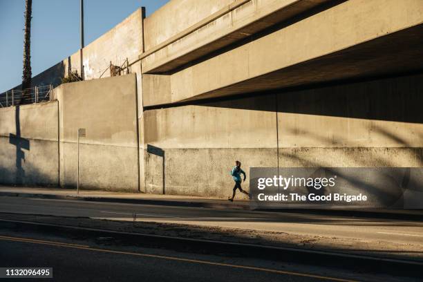 woman running under bridge on sidewalk in city - street side stock-fotos und bilder