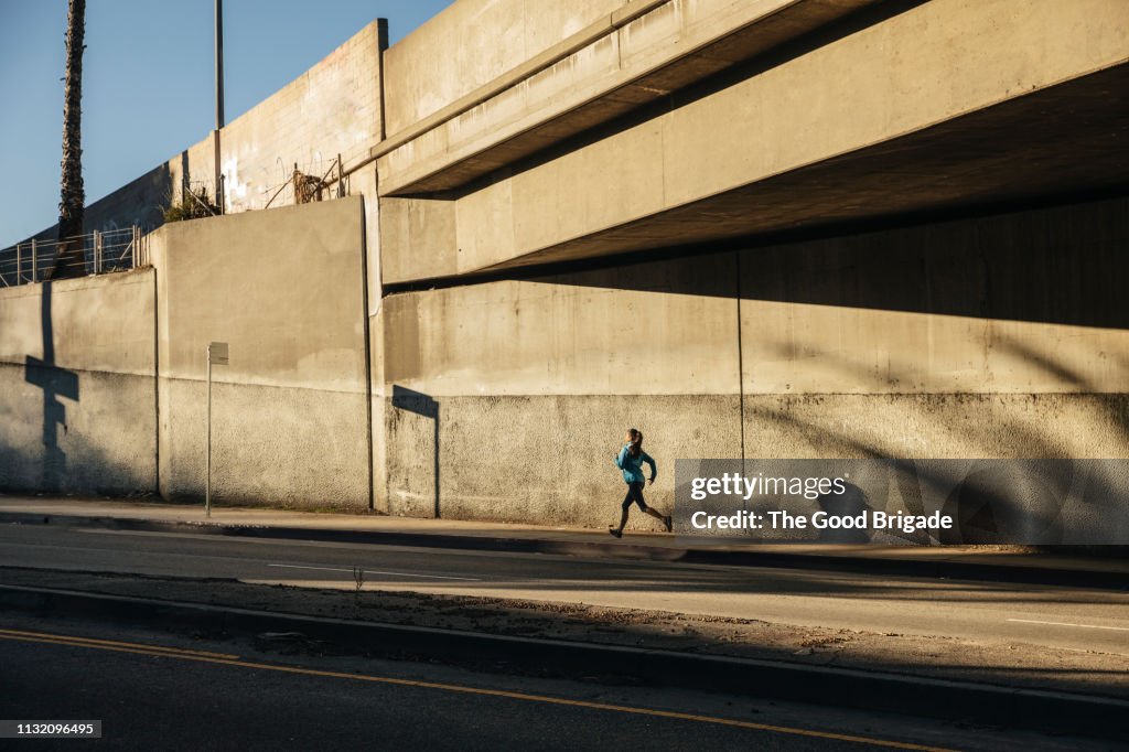 Woman running under bridge on sidewalk in city