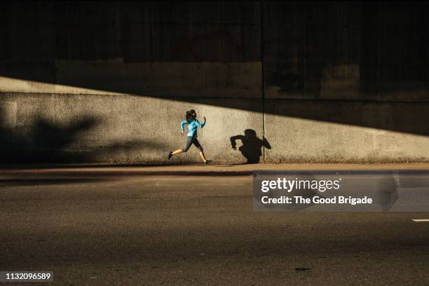 woman running against wall on city street - urban running foto e immagini stock