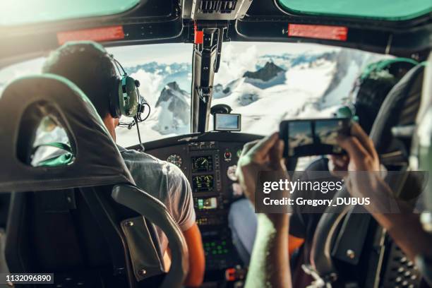 interior of helicopter cockpit with unrecognizable pilot and defocused tourist taking photos of the flight over mont blanc massif - haute savoie stock pictures, royalty-free photos & images