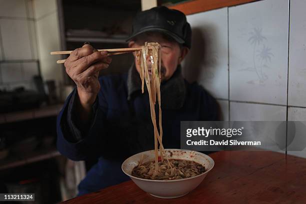 Chinese man eats noodles in a spicy sauce at a small traditional restaurant in the local market on December 2, 2010 in Gu Cheng in China's Sichuan...