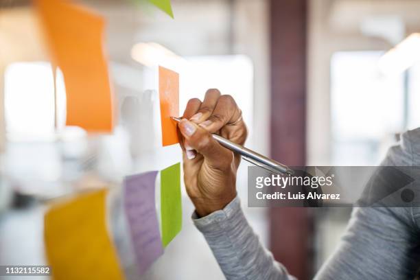 female writing new ideas on sticky note - strategy foto e immagini stock