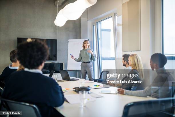 businesswoman addressing a meeting around board table - directeur photos et images de collection