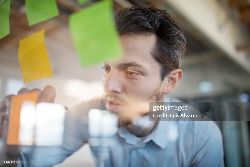 Young businessman writing on adhesive note