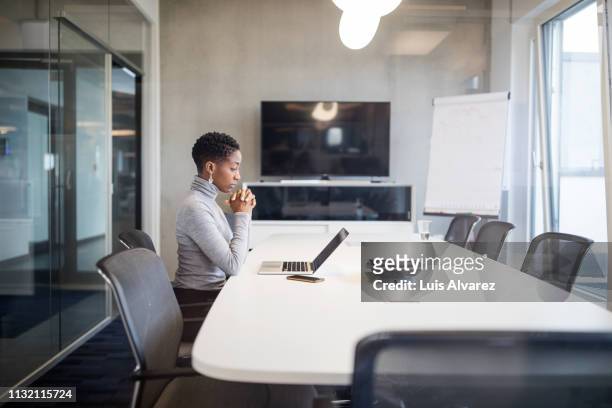 businesswoman sitting at conference table with on laptop - mid adult stock-fotos und bilder