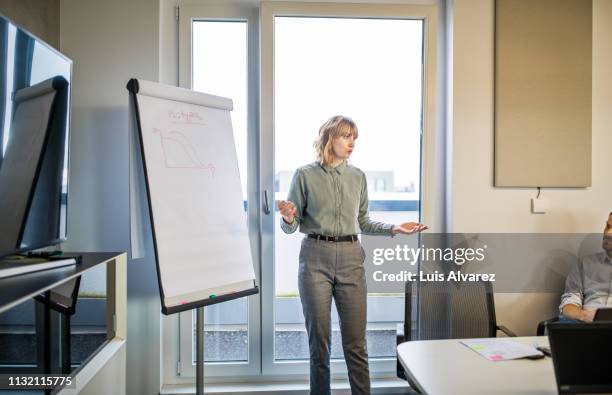 businesswoman standing by a flip chart giving presentation - woman whiteboard fotografías e imágenes de stock