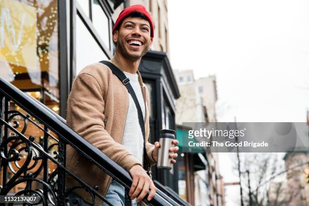 smiling young man walking down stairs in city - borsa messenger foto e immagini stock