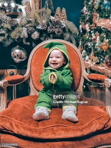 Smiling newborn baby in cute green outfit clapping in red chair.