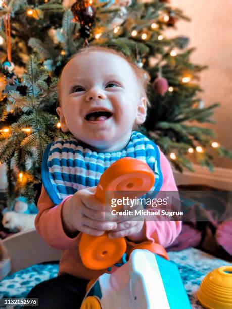 Smiling newborn baby in front of Christmas tree.
