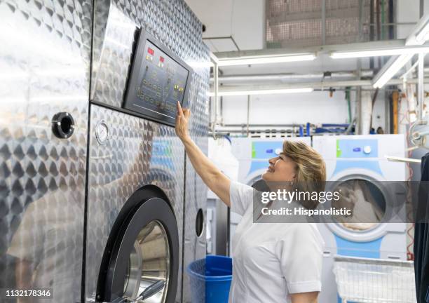 mature woman working at a laundry service operating an industrial washing machine smiling - lavandaria imagens e fotografias de stock