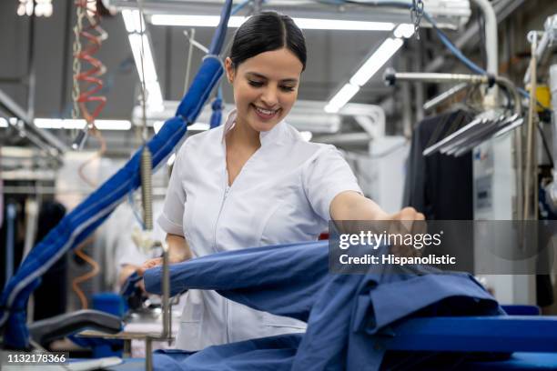 mujer joven latinoamericana trabajando en una lavandera ropa de planchado sonriendo - laundromat fotografías e imágenes de stock