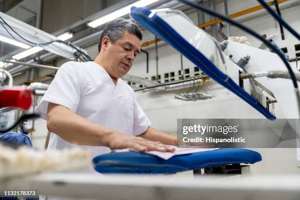 latin american mature man at a laundromat ironing clothes with a steamer - dry cleaning shop stock pictures, royalty-free photos & images