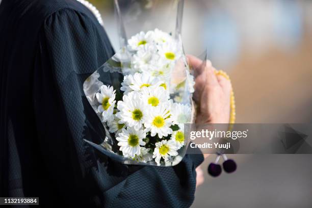 葬儀と日本の墓への訪問.シニアの女性は、黒い喪服で先祖の魂を崇拝します。私は手に白い菊の束とビーズを保持しています。 - 墓所 ストックフォトと画像