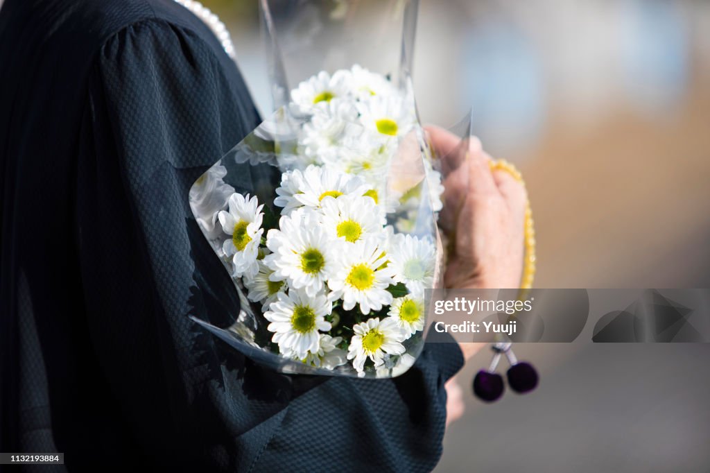 Een begrafenis en bezoek aan een graf van Japan. De vrouw van de Senior verering van de voorouderlijke ziel in een zwarte rouw jurk. Ik houd witte chrysant stelletje en kralen in een hand.