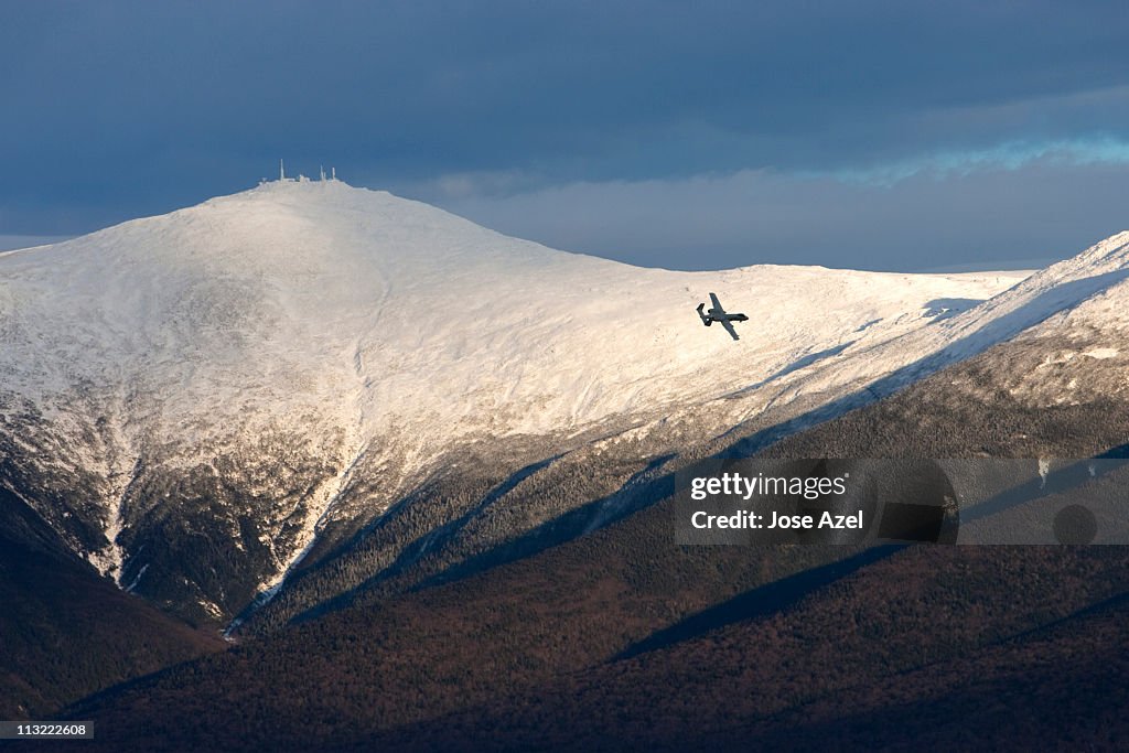 A plane flies in the distance over Mt. Washington and the Presidential Range .