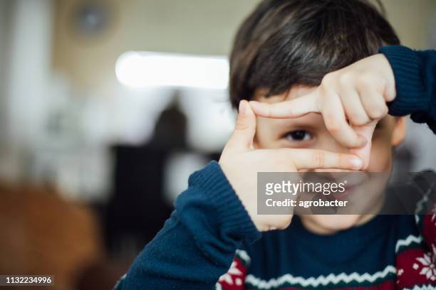 o menino faz um frame do dedo em torno de seu olho - dedos fazendo moldura - fotografias e filmes do acervo