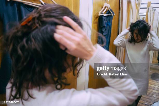 young woman touching her hair and looking at the mirror in the changing room - anprobekabine stock-fotos und bilder