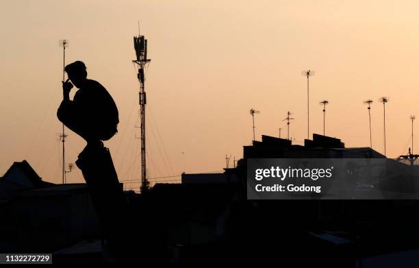 Silhouette of young man against sunset sky and roof house. Cai Be. Vietnam.
