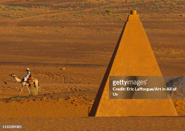 Sudanese man and his camel in front of the pyramids of the kushite rulers at Meroe, Northern State, Meroe, Sudan on December 28, 2018 in Meroe, Sudan.