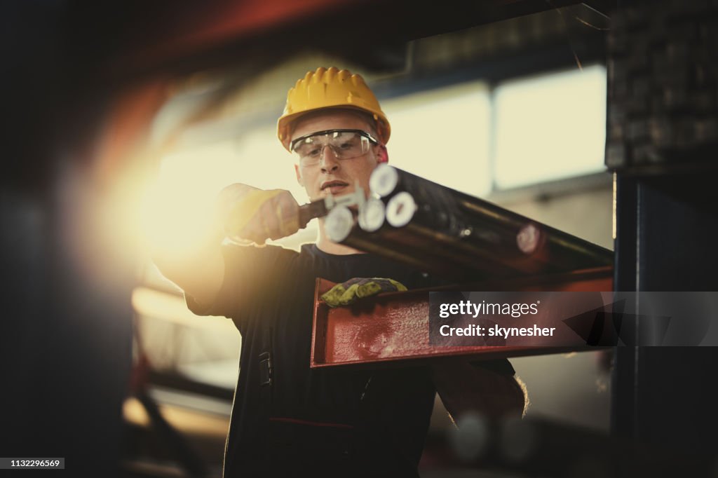 Trabajador manual joven que mide el tubo de acero con el calibrador en molino de aluminio.