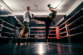 Powerful caucasian boxer girl in sportswear, with bandage on feet and boxing gloves on hands practicing with trainer in ring.