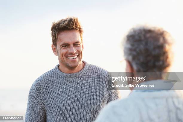 mature son talking to his senior father at sunset at the beach - father and son discussion stock-fotos und bilder