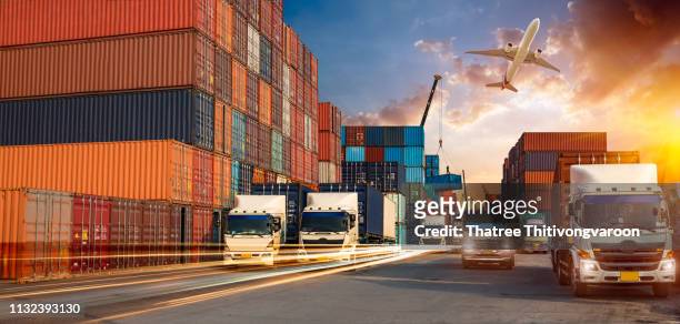 container truck in ship port for business logistics and transportation of container cargo ship and cargo plane with working crane bridge in shipyard at sunrise, logistic import export and transport industry background - cargo plane stock-fotos und bilder