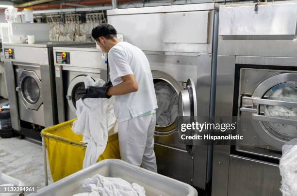 latin american man loading washing machine with dirty bed sheets at an industrial laundry service - dry cleaning shop stock pictures, royalty-free photos & images