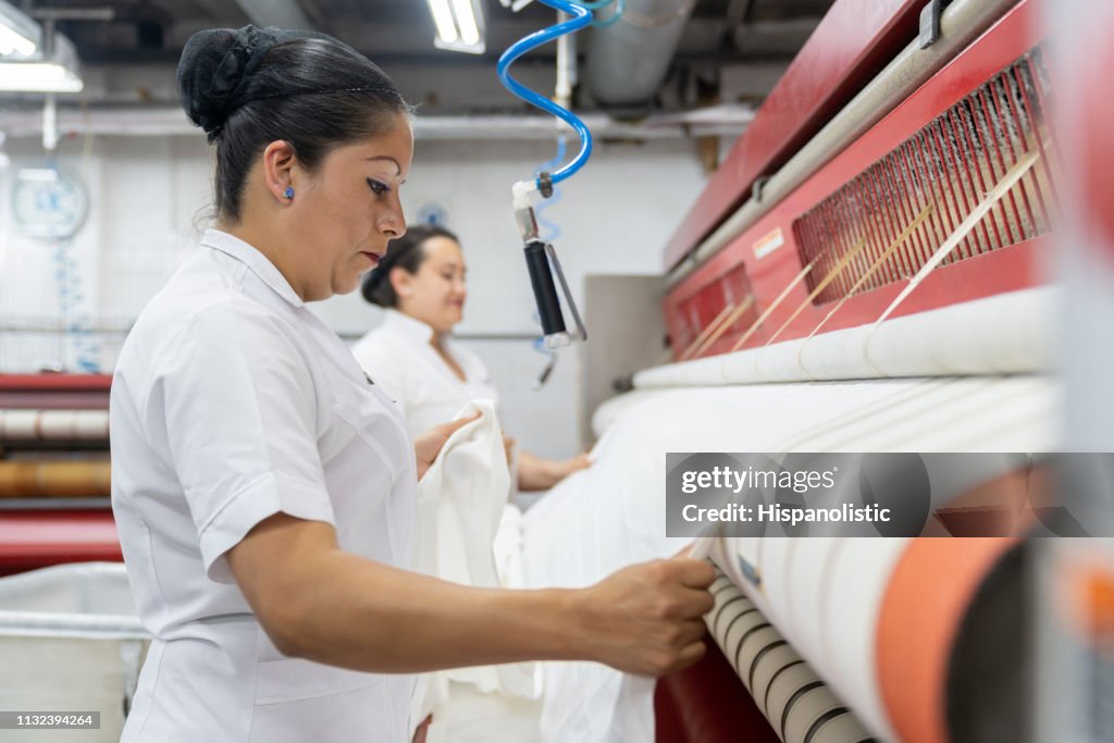 Latin american females ironing sheets with an industrial iron