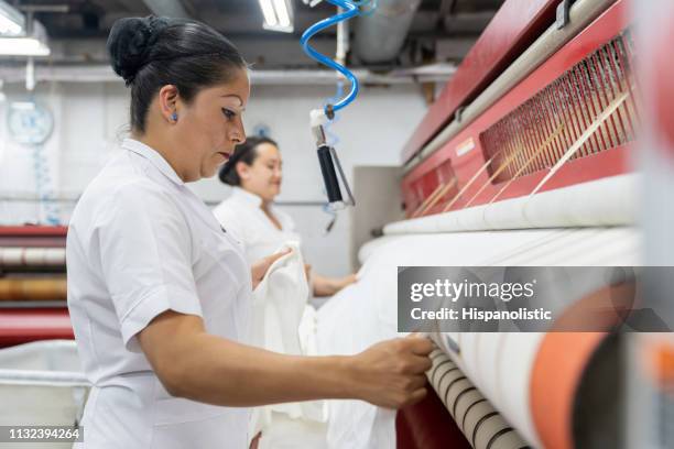 latin american females ironing sheets with an industrial iron - bedclothes stock pictures, royalty-free photos & images