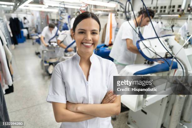 hermoso latino americano joven supervisor en un servicio de lavandería industrial sonriendo a la cámara con los brazos cruzados - laundromat fotografías e imágenes de stock