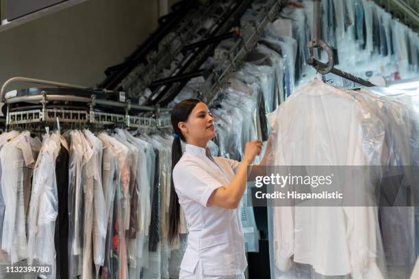 beautiful woman at an industrial laundry looking for a dry cleaned garment on conveyor belt - dry cleaned stock pictures, royalty-free photos & images