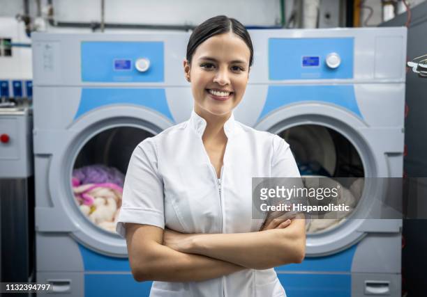 confident latin american female supervisor at a laundromat with arms crossed facing camera smiling - laundromat stock pictures, royalty-free photos & images