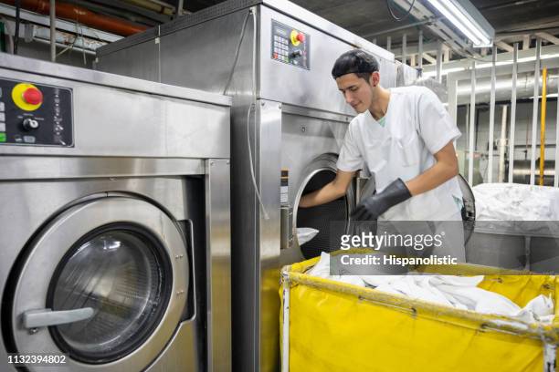 homme focalisé travaillant à un service de blanchisserie industriel chargeant la machine à laver portant des gants de protection - dry cleaning photos et images de collection