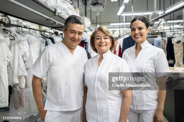 portrait of employees at a laundry service wearing uniform smiling at camera - dry cleaning shop stock pictures, royalty-free photos & images