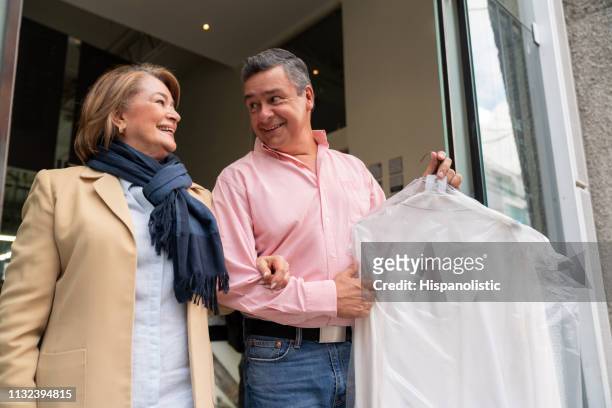 loving couple looking at each other talking while man holds their dry cleaned garments - dry cleaned stock pictures, royalty-free photos & images