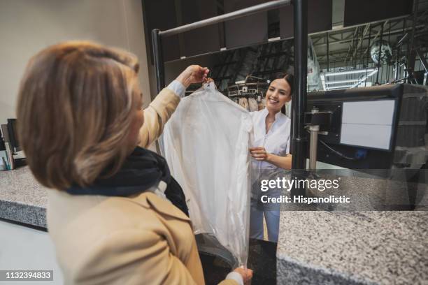 vrouwelijke klant plukken haar droge kleren schoongemaakt van wasservice, terwijl ze glimlacht en handen kledingstuk op kleerhanger - dry cleaning stockfoto's en -beelden