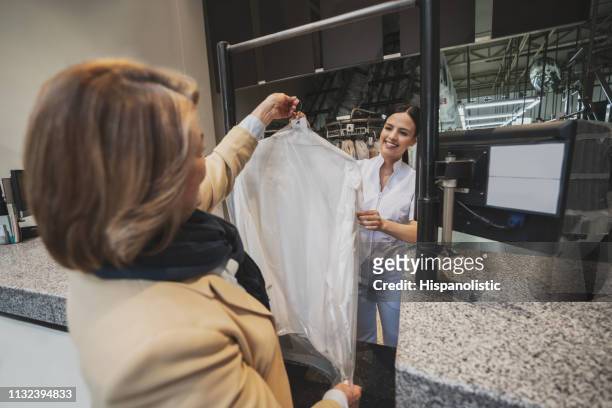 female customer picking her dry cleaned clothes from laundry service while she smiles and hands garment on coat hanger - dry cleaning stock pictures, royalty-free photos & images
