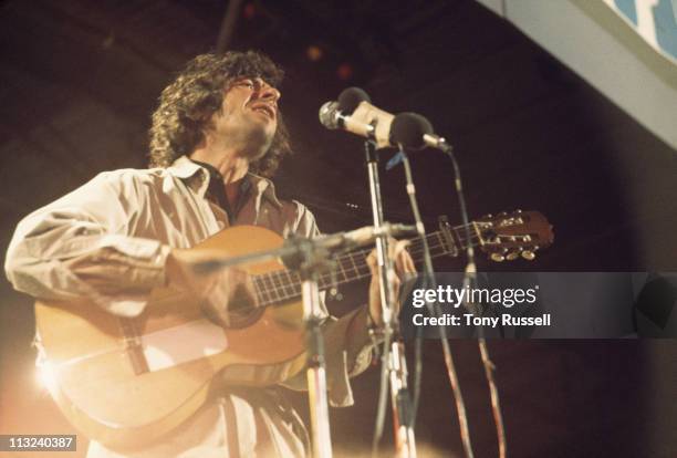 Leonard Cohen, Canadian singer-songwriter, musician and poet, playing the guitar and singing into a microphone during a live concert performance at...