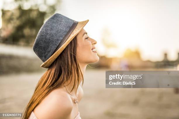 feliz joven mujer hipster día soñando en una hermosa puesta de sol en la ciudad. - sombrero mujer fotografías e imágenes de stock