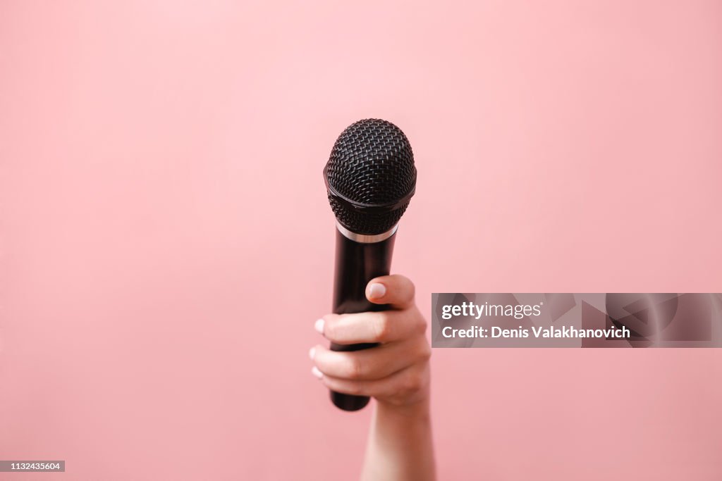 Microphone in female hand on pink background