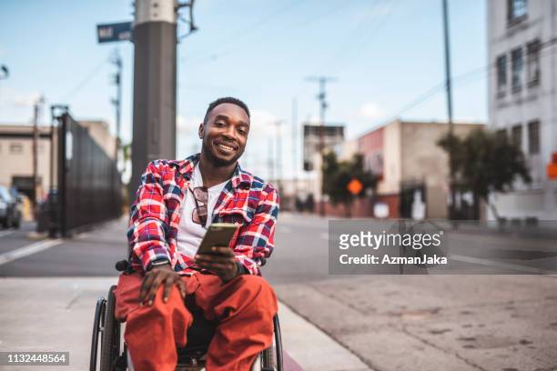 portret van een afro-amerikaanse gehandicapte mannen in een rolstoel met behulp van slimme telefoon buitenshuis - wheelchair stockfoto's en -beelden