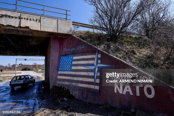 Car drives past a graffiti reading 'Thank You Nato' and featuring the US flag near the village of Stagovo on March 24, 2019. - 20 years ago, NATO...