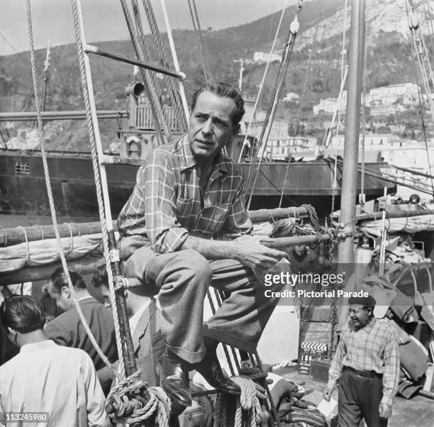 American actor Humphrey Bogart sitting on the rigging of a boat during filming of the 1953 film 'Beat the Devil' in Italy.