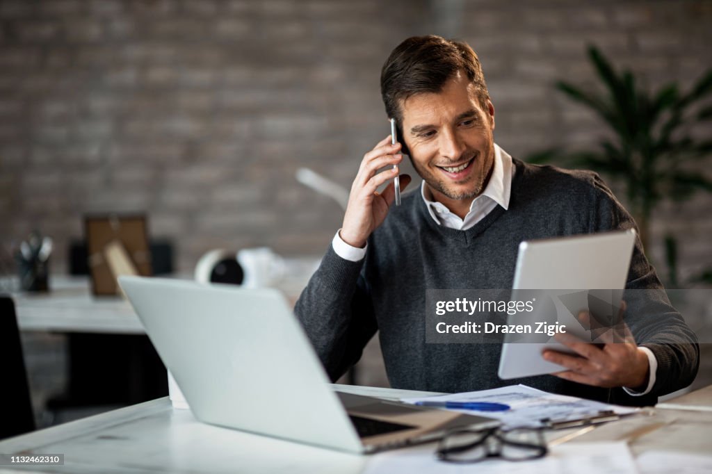 Hombre de negocios feliz usando tableta digital mientras habla en el teléfono celular en la oficina.