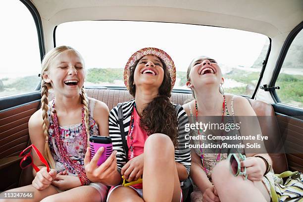 three girls laughing in the back seat of a vehicle - kids fashion stockfoto's en -beelden