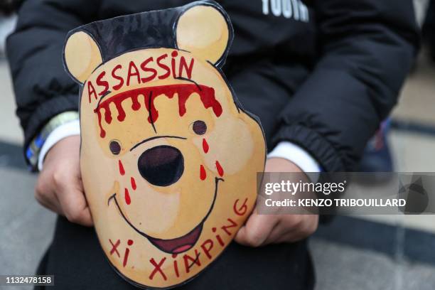 Demonstrator holds a cardboard mask depicting Winnie-the-Pooh with the message 'Xi Jinping murderer' during a march of the Tibetan community in...