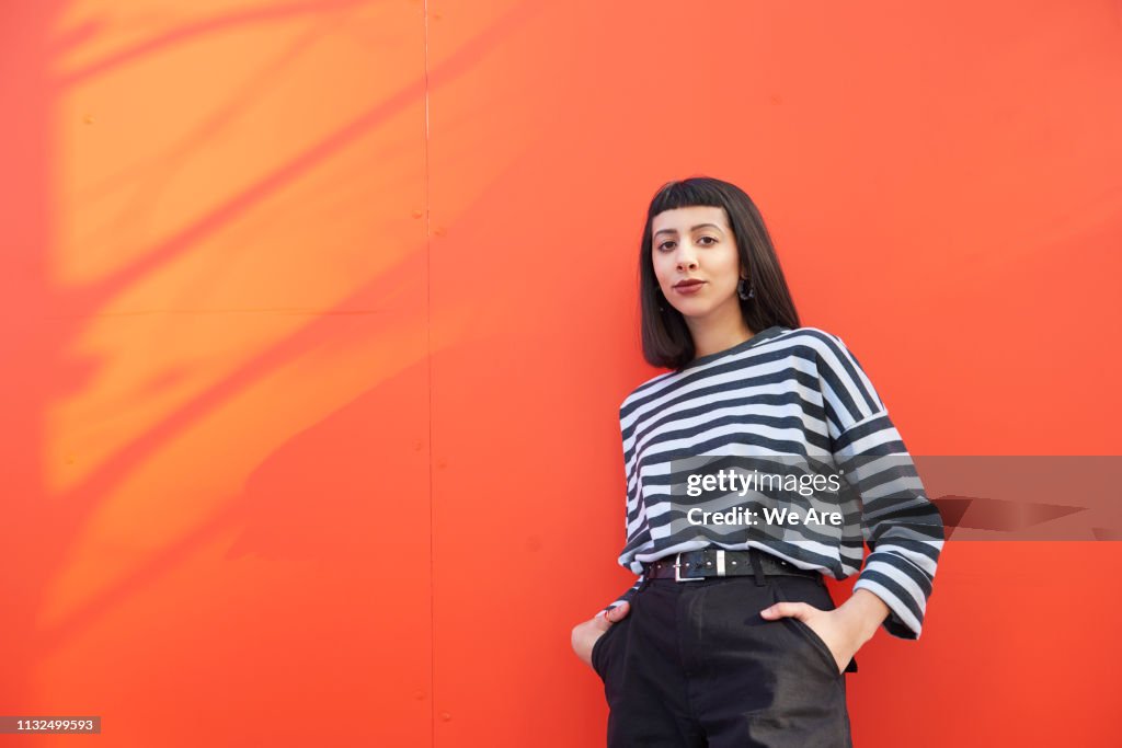 Portrait of young woman standing against red background.