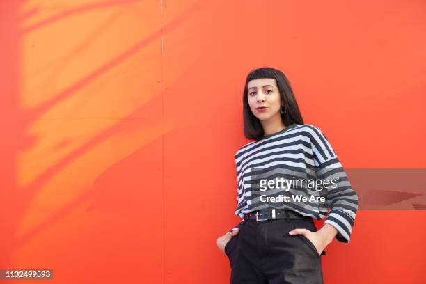 portrait of young woman standing against red background. - cool attitude stockfoto's en -beelden