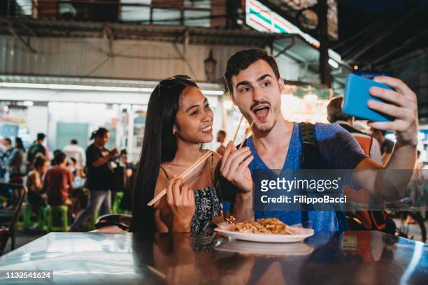 junges paar beim gemeinsamen abendessen auf dem nachtmarkt und ein selfie - foodie stock-fotos und bilder